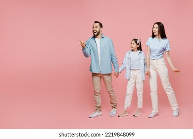 Full body young happy parents mom dad with child kid daughter teen girl in blue clothes hold hands walk going point index finger aside on workspace area isolated on plain pastel light pink background. - Shutterstock ID 2219848099