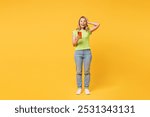 Full body young happy shocked surprised blonde woman wear green t-shirt casual clothes put arm on head hold in hand use mobile cell phone isolated on plain yellow orange background. Lifestyle concept