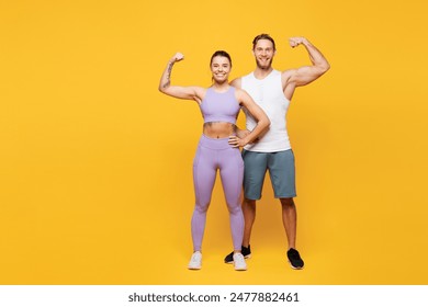 Full body young happy strong fitness trainer sporty two man woman wearing blue clothes spend time in home gym show muscles biceps on hand isolated on plain yellow background. Workout sport fit concept - Powered by Shutterstock