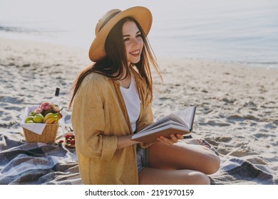 Full body young happy traveler tourist woman in straw hat shirt summer clothes reading book sit on plaid have picnic outdoors on sea sand beach background People vacation lifestyle journey concept.