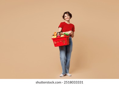 Full body young happy woman she wear red t-shirt casual clothes hold basket bag with food products look camera isolated on plain pastel light beige background. Delivery service from shop or restaurant - Powered by Shutterstock