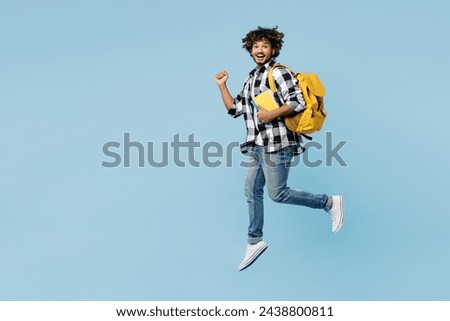 Full body young Indian boy student wear shirt casual clothes backpack bag hold books jump high do winner gesture isolated on plain pastel light blue background. High school university college concept