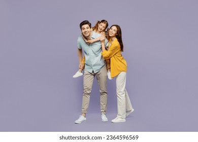 Full body young joyful happy parents mom dad with child kid daughter girl 6 years old wear blue yellow casual clothes giving piggyback ride to joyful, sit on back isolated on plain purple background