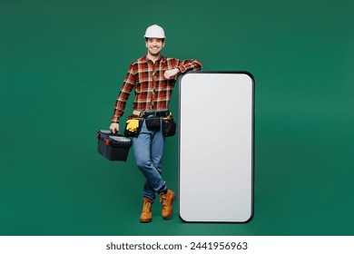 Full body young laborer man wear red shirt hardhat big huge blank screen area mobile cell phone hold toolbox isolated on plain green background. Instruments for renovation room. Repair home concept - Powered by Shutterstock