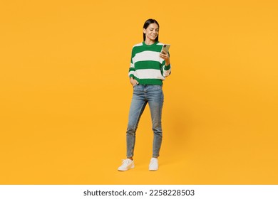 Full body young latin woman wear casual green knitted sweater hold in hand use mobile cell phone chatting online surfing internet isolated on plain yellow background studio People lifestyle concept - Powered by Shutterstock