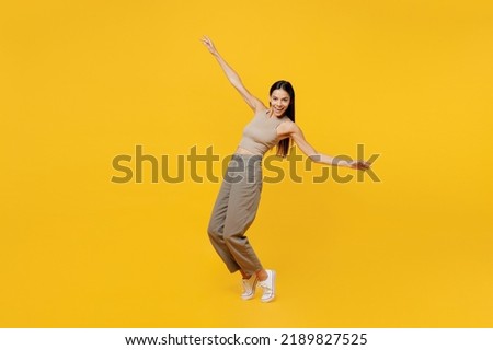 Full body young latin woman 30s she wear basic beige tank shirt stand on toes leaning back dance with outstretched hands isolated on plain yellow backround studio portrait. People lifestyle concept