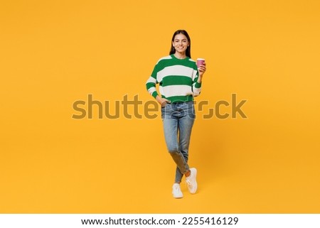 Full body young latin woman wearing casual cozy green knitted sweater hold takeaway delivery craft paper cup coffee to go isolated on plain yellow background studio portrait People lifestyle concept