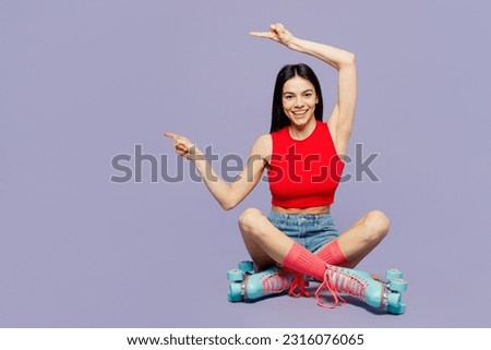 Full body young latin woman she wear red casual clothes rollers rollerblading poin finger aside on copy space area mock up isolated on plain purple background. Summer sport lifestyle leisure concept