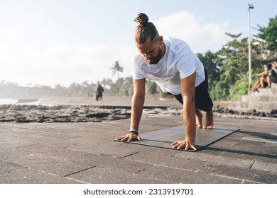 Full body of young male athlete performing Surya Namaskar in stages while training on embankment near waving sea in morning sun time - Powered by Shutterstock