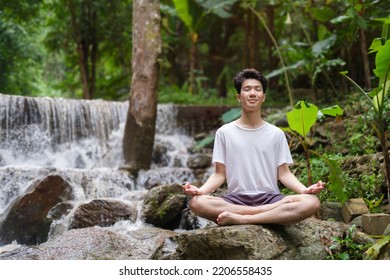 Full Body Young Male In Casual Clothes Sitting On Stone Edge In Lotus Pose. Sport, Yoga, Pilates, Fitness, Healthy Lifestyle Concept.