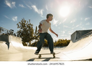 Full body of young male skater in casual outfit doing trick on skateboard riding in skate park