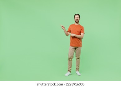 Full body young man 20s wear casual orange t-shirt point index finger aside on workspace area mock up isolated on plain pastel light green color background studio portrait. People lifestyle concept - Shutterstock ID 2223916335