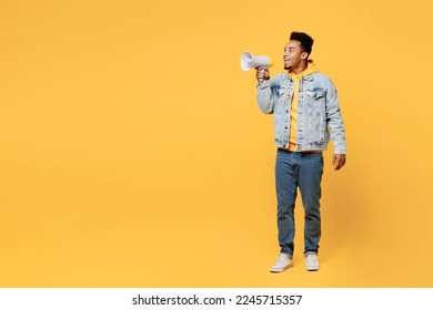 Full body young man of African American ethnicity wear denim jacket hoody hold in hand megaphone scream announces discounts sale Hurry up look aside on area isolated on plain yellow background studio - Shutterstock ID 2245715357