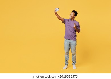 Full body young man of African American ethnicity wears t-shirt casual clothes do selfie shot on mobile cell phone post photo on social network isolated on plain yellow background. Lifestyle concept