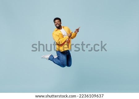 Full body young man of African American ethnicity 20s he wear yellow shirt jump high point index finger aside on workspace area isolated on plain pastel light blue background. People lifestyle concept