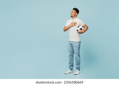 Full body young man fan wearing t-shirt cheer up support football sport team hold in hand soccer ball watch tv live stream sing national country anthem isolated on plain pastel blue color background - Powered by Shutterstock