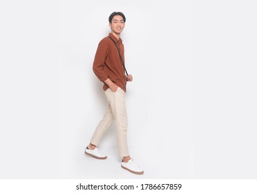 Full Body Young Man In Khakis And Long Sleeve Brown Shirt Standing With White Sneakers Runway In Studio
