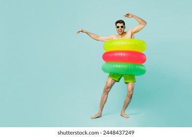 Full body young man wear green shorts swimsuit glasses relax near hotel pool in three inflatable rings dance raise up hands isolated on plain blue background. Summer vacation sea rest sun tan concept - Powered by Shutterstock