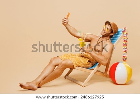 Full body young man wear yellow shorts swimsuit relax rest near hotel pool sit in deckchair do selfie shot on mobile cell phone isolated on plain beige background. Summer vacation sea sun tan concept