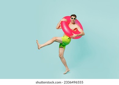 Full body young man wears green shorts swimsuit glasses relax near hotel pool hold inflatable ring lean back raise up leg isolated on plain blue background. Summer vacation sea rest sun tan concept - Powered by Shutterstock