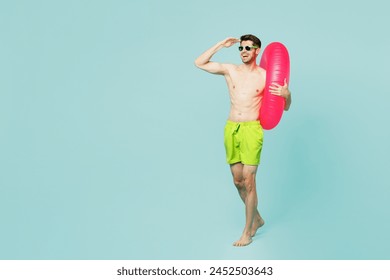 Full body young man wears green shorts swimsuit glasses relax near hotel pool hold inflatable ring look far away distance isolated on plain blue background. Summer vacation sea rest sun tan concept - Powered by Shutterstock