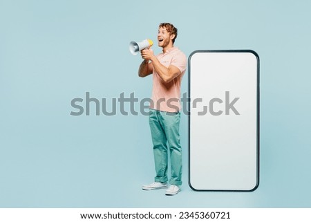 Full body young man wears pink t-shirt casual clothes big huge blank screen mobile cell phone smartphone with workspace area scream in megaphone isolated on plain blue background. Lifestyle concept