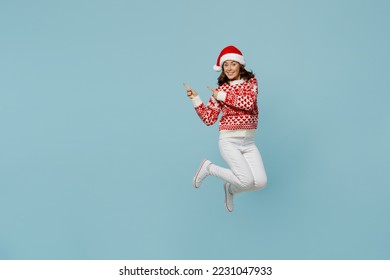 Full body young merry woman wear red knitted sweater Santa hat posing jump high point indicate on workspace area isolated on plain pastel light blue cyan background Happy New Year 2023 holiday concept - Powered by Shutterstock