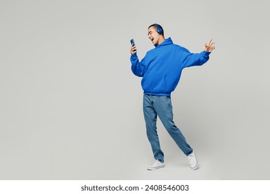 Full body young middle eastern man he wears blue hoody casual clothes listen to music in headphones use mobile cell phone isolated on plain solid white background studio portrait. Lifestyle concept - Powered by Shutterstock