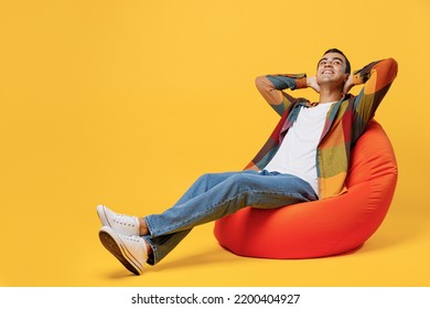 Full body young minded fun middle eastern man wear casual shirt white t-shirt sit in bag chair hold hands behind neck look overhead isolated on plain yellow background studio People lifestyle concept - Powered by Shutterstock