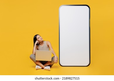 Full Body Young Minded Latin Woman She Wear Tank Shirt Near Big Huge Blank Screen Mobile Cell Phone With Workspace Copy Space Hold Use Work On Laptop Pc Computer Isolated On Plain Yellow Backround.