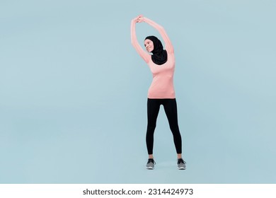 Full body young muslim fitness trainer sporty woman wear pink abaya hijab spend time in home gym train do stretch lunge exercise rising hands up isolated on plain blue background Sport fit abs concept - Powered by Shutterstock