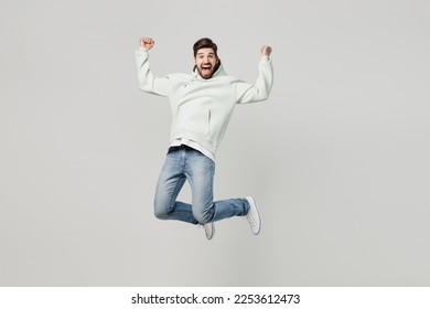 Full body young overjoyed excited satisfied fun caucasian man wear mint hoody look camera jump high do winner gesture isolated on plain solid white background studio portrait. People lifestyle concept - Shutterstock ID 2253612473