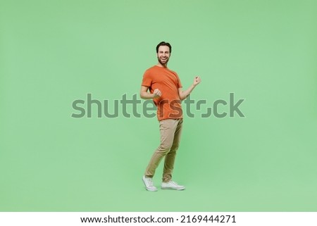 Full body young overjoyed excited happy cool fun man 20s wear casual orange t-shirt he do winner gesture isolated on plain pastel light green color background studio portrait. People lifestyle concept