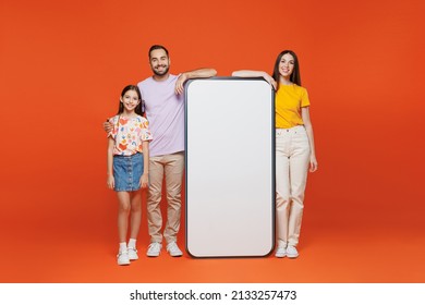 Full Body Young Parents Mom Dad With Child Kid Daughter Teen Girl In Basic T-shirts Big Blank Screen Mobile Cell Phone With Copy Space Mockup Area Isolated On Yellow Background. Family Day Concept.