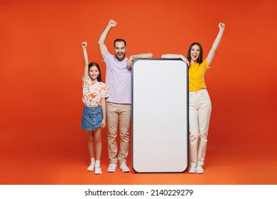 Full Body Young Parents Mom Dad With Child Kid Daughter Teen Girl Wear Basic T-shirts Big Blank Screen Mobile Cell Phone With Mockup Do Winner Gesture Isolated On Yellow Background Family Day Concept.