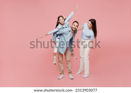 Full body young parents mom dad with child kid daughter teen girl in blue clothes give piggyback ride to kid sit on back stretch hands isolated on plain pastel light pink background Family day concept