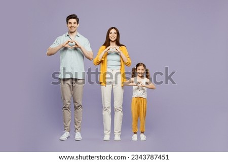 Full body young parents mom dad with child kid daughter girl 6 years old wear yellow casual clothes show shape heart with hands heart-shape sign isolated on plain purple background. Family day concept