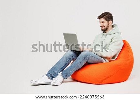 Full body young programmer happy caucasian IT man wear mint hoody sit in bag chair hold use work on laptop pc computer isolated on plain solid white background studio portrait People lifestyle concept