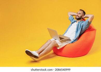 Full Body Young Relaxed Happy Man 20s Wear Blue Shirt White T-shirt Sit In Bag Chair Hold Use Work On Laptop Pc Computer Hold Hands Behind Neck Head Isolated On Plain Yellow Background Studio Portrait