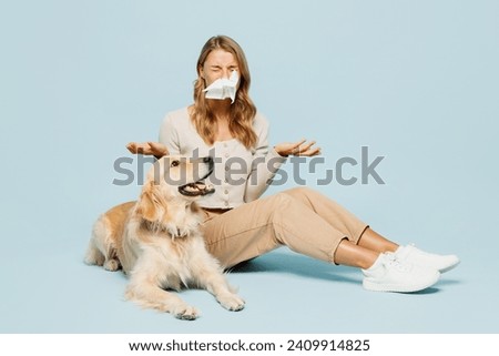 Full body young sick ill sad owner woman wears casual clothes sit near her best friend retriever dog blow nose using napkin isolated on plain light blue background studio. Allergy health care concept