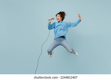 Full body young singer happy woman wear knitted sweater jump high sing song in microphone raise up hand isolated on plain pastel light blue cyan background studio portrait. People lifestyle concept - Powered by Shutterstock