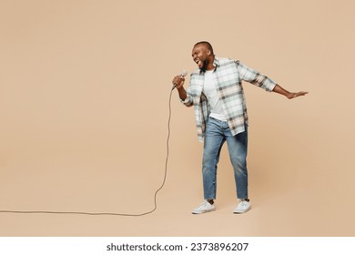 Full body young singer man of African American ethnicity he wear light shirt casual clothes sing song in microphone at karaoke club isolated on plain pastel beige background studio. Lifestyle concept - Powered by Shutterstock