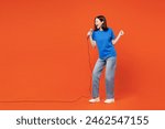 Full body young singer smiling happy woman she wearing blue t-shirt casual clothes sing song in microphone at karaoke club isolated on plain red orange background studio portrait. Lifestyle concept