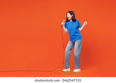 Full body young singer smiling happy woman she wearing blue t-shirt casual clothes sing song in microphone at karaoke club isolated on plain red orange background studio portrait. Lifestyle concept - Powered by Shutterstock