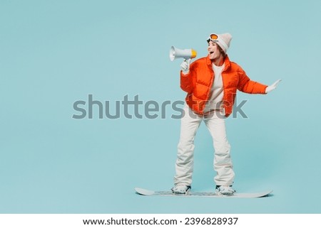 Full body young skier woman wear warm padded windbreaker jacket hat ski goggles mask scream shout in megaphone travel rest spend weekend winter season in mountains isolated on plain blue background
