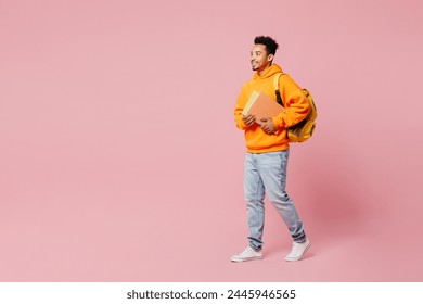 Full body young smart student man of African American ethnicity wear yellow hoody casual clothes backpack bag hold books walk go isolated on plain pastel pink background High school university concept - Powered by Shutterstock