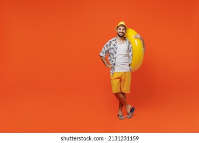 Full body young smiling cheerful fun cool tourist man wear beach shirt hat hold inflatable ring look camera isolated on plain orange background studio portrait Summer vacation sea rest sun tan concept