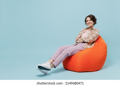 Full Body Young Smiling Cheerful Happy Woman 20s Wearing Casual Brown Shirt Sit In Bag Chair Look Camera Isolated On Pastel Plain Light Blue Color Background Studio Portrait. People Lifestyle Concept