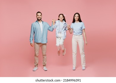 Full Body Young Smiling Cool Happy Parents Mom Dad With Child Kid Daughter Teen Girl In Blue Clothes Hold Hands Jump High Have Fun Isolated On Plain Pastel Light Pink Background. Family Day Concept