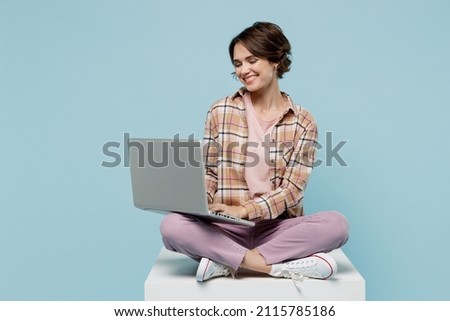 Full body young smiling copywriter happy cool woman 20s wear brown shirt sit on white chair hold use work on laptop pc computer isolated on pastel plain light blue b ackground People lifestyle concept